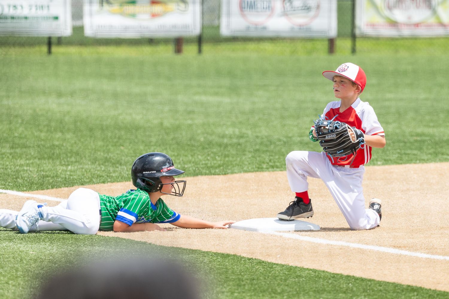 Two young boys playing little league baseball, one sliding into base while the other holds a glove ready to make the tag.
