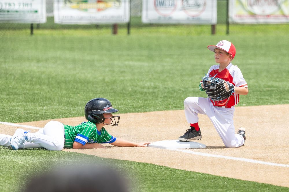 Two young boys playing little league baseball, one sliding into base while the other holds a glove ready to make the tag.