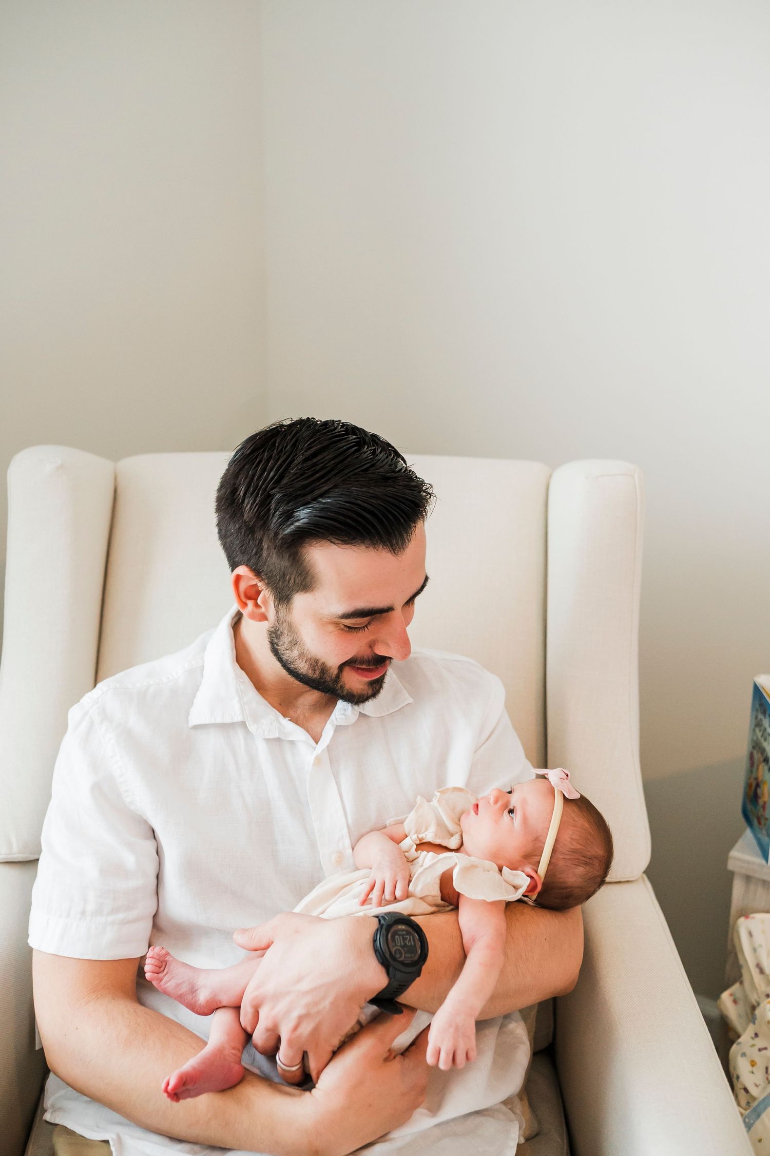 A person in a white shirt cradles a small baby while sitting in a plush cream-colored chair.