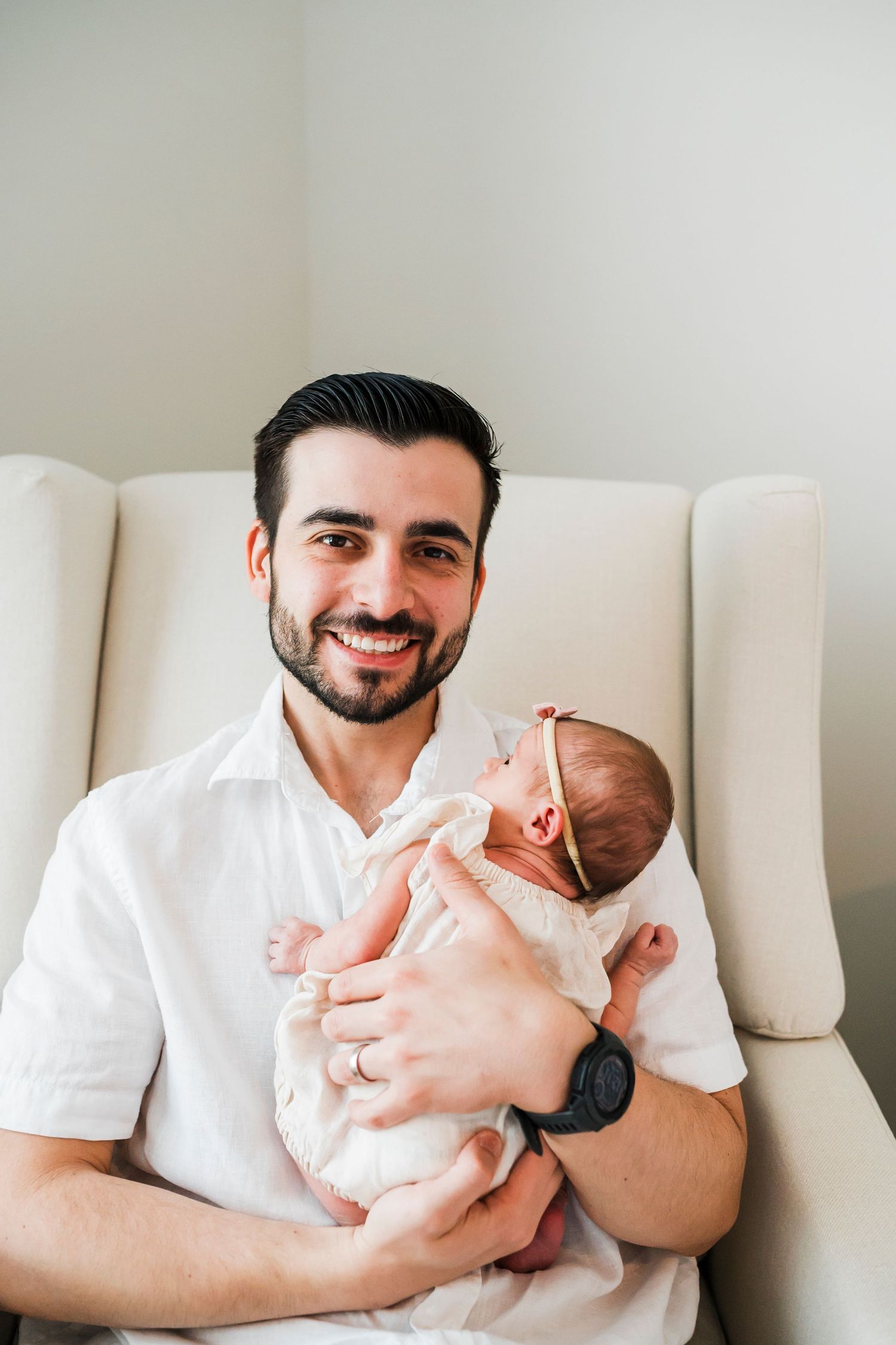 Tender moment between a caregiver in a white shirt and a newborn baby in a cozy white setting with natural light.