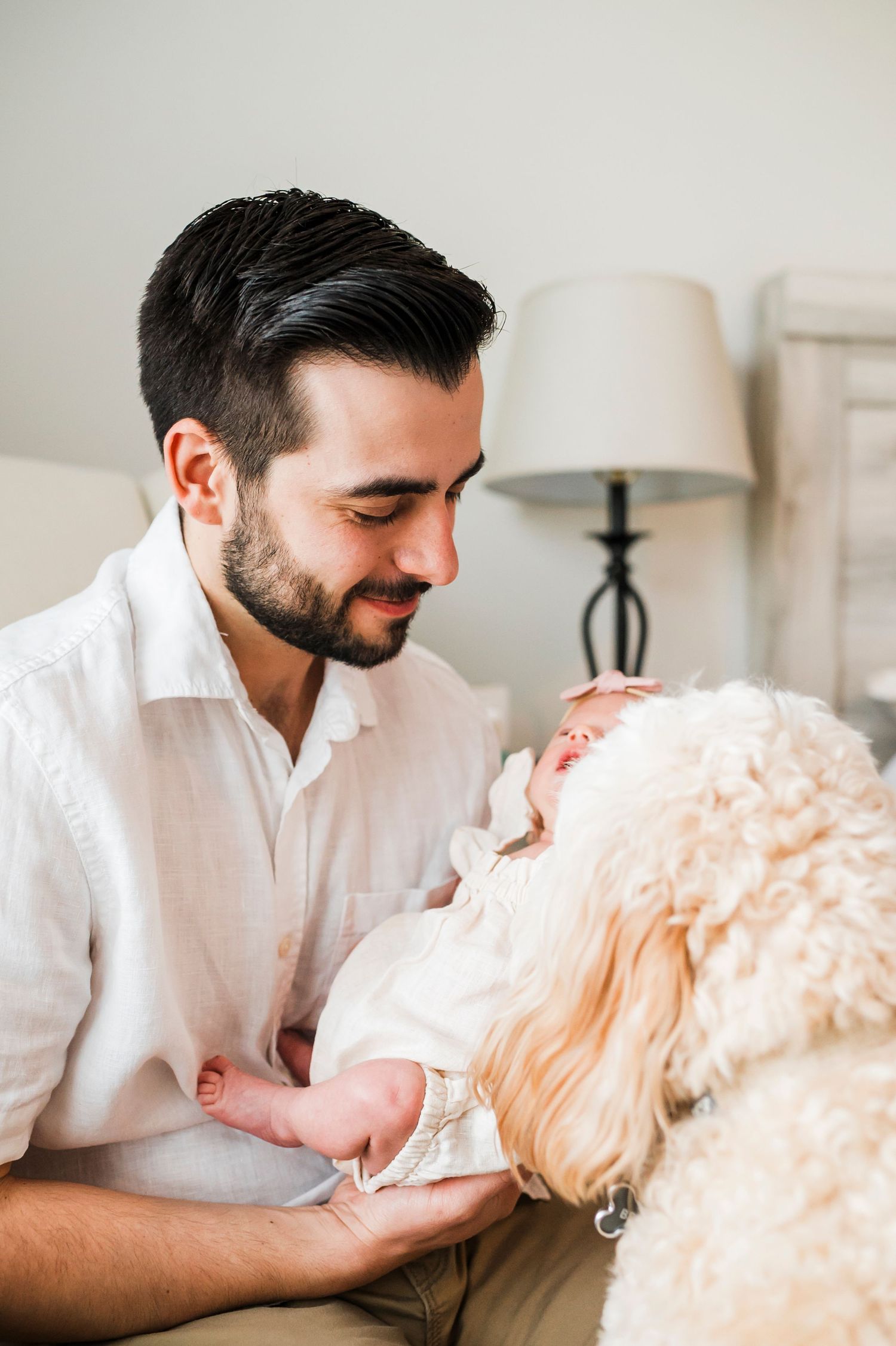 A tender moment shared between couple and newborn on a white bed with delicate lighting.