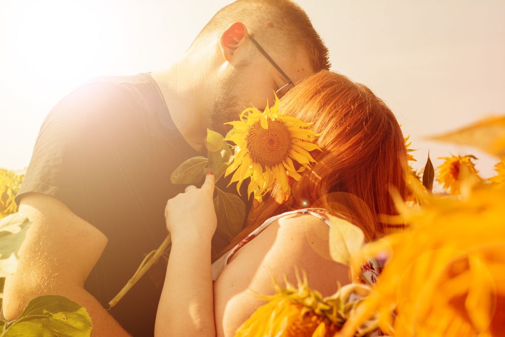 A romantic couple embraces in a dreamy sunlit field of bright yellow sunflowers at golden hour.