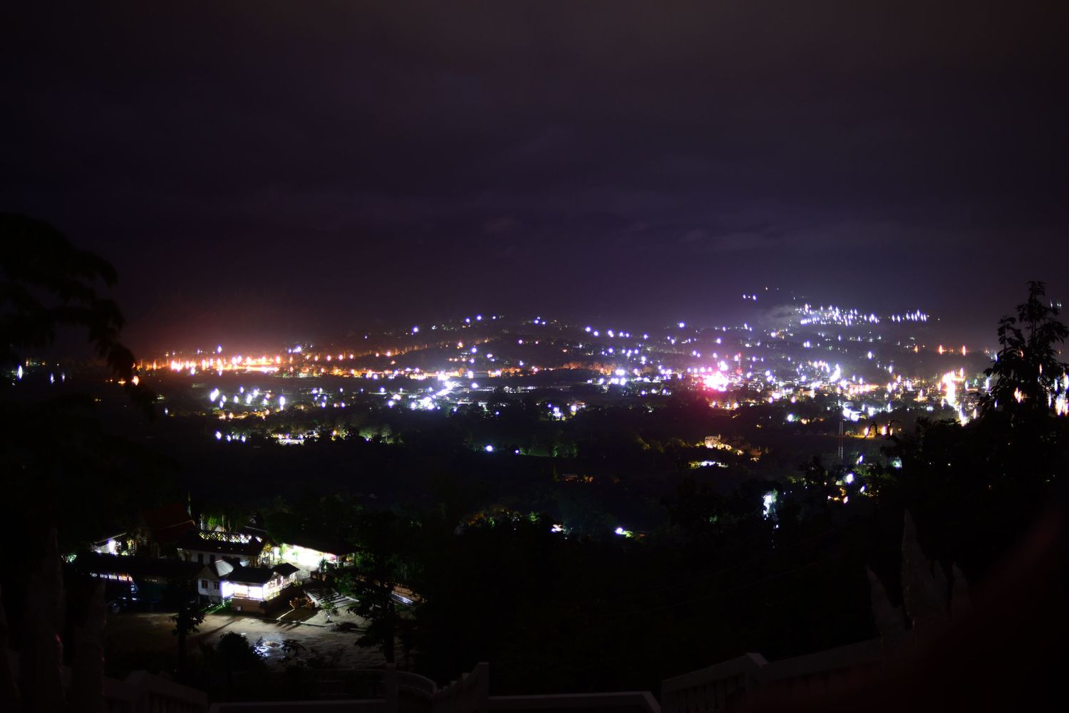 Cityscape panorama of lights twinkling across a darkened hillside and valley at night.