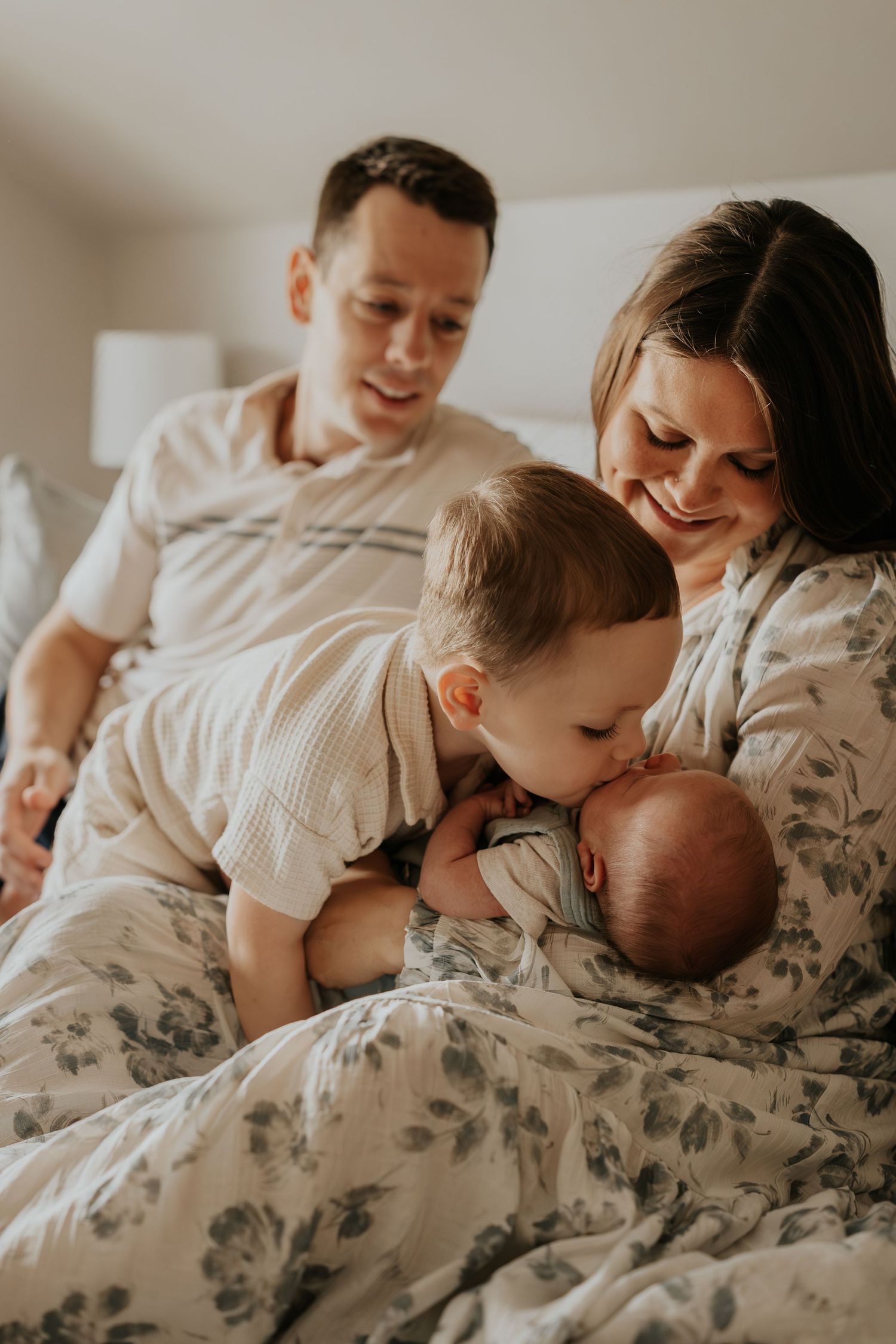 A young family sharing an intimate moment together on a bed with floral bedding as they bond with their newborn baby.