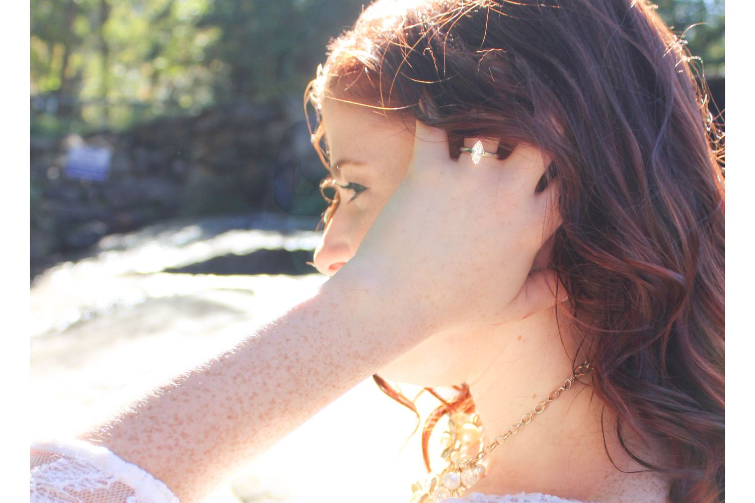 Close up profile portrait with sunlit hair and natural waterfall backdrop.