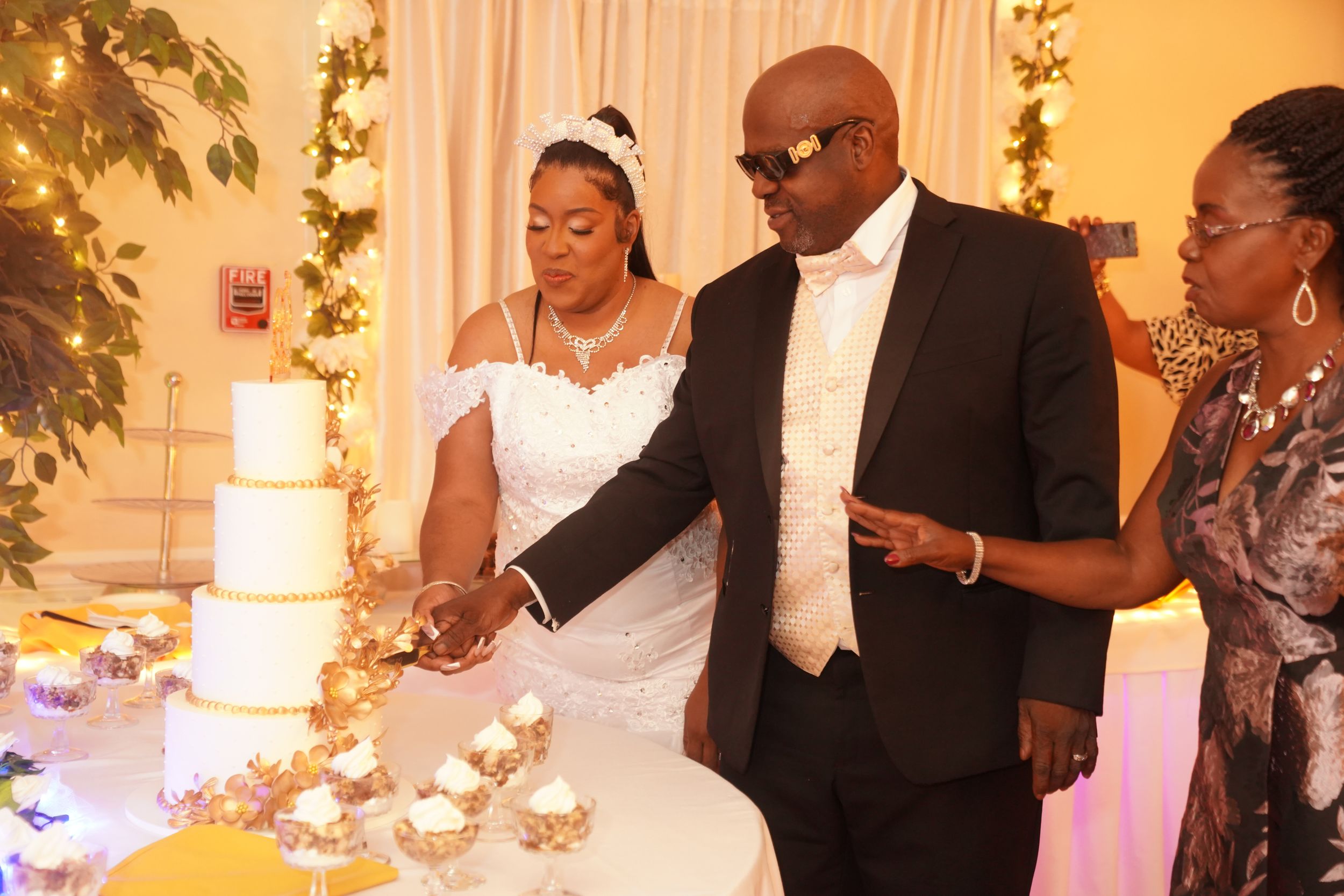 A wedding reception cake cutting ceremony in a beautifully decorated ballroom with warm lighting and floral arrangements.