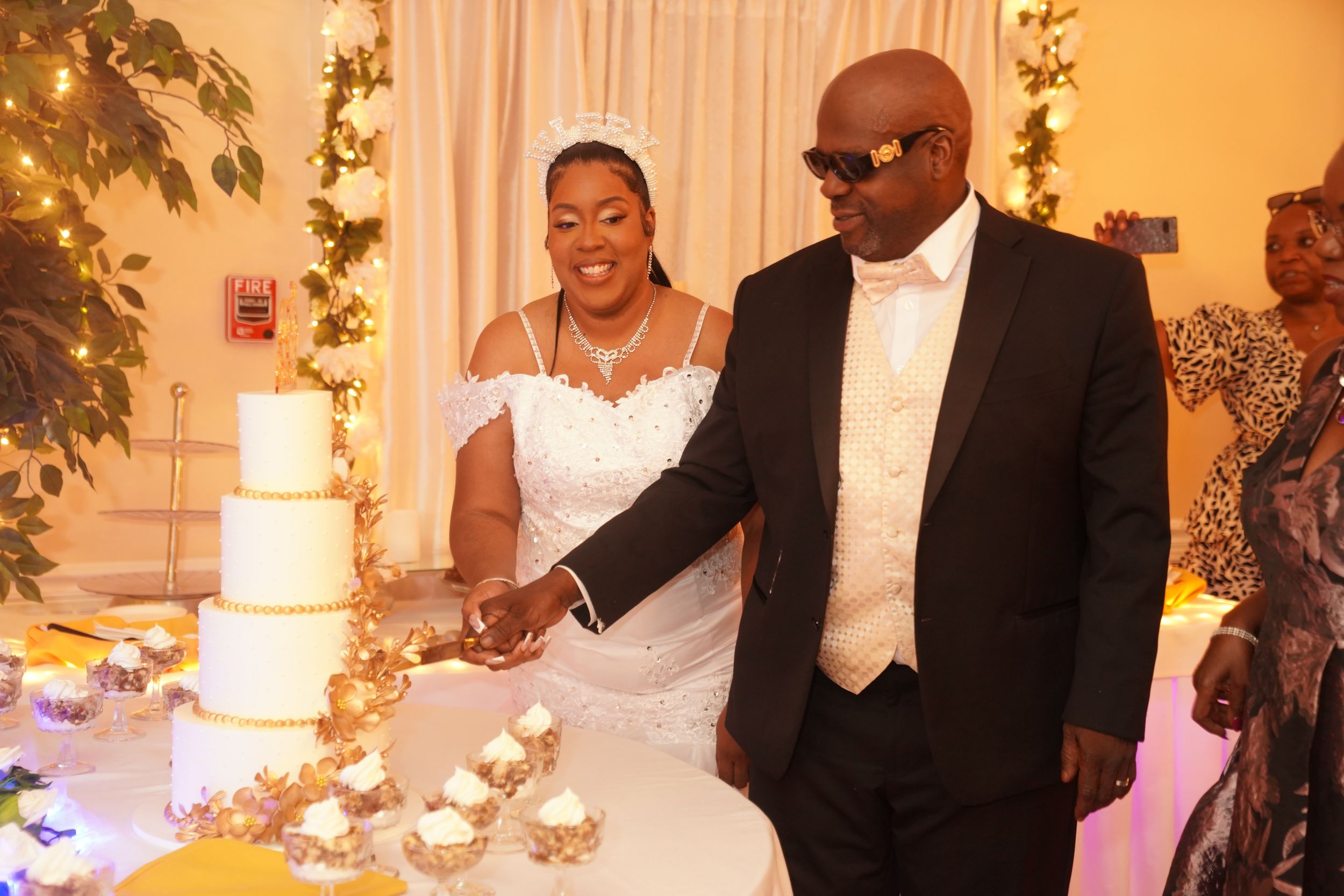 A couple cuts their elegant white wedding cake together at their reception in a warm, ambient-lit setting.