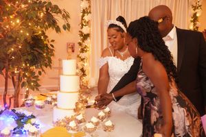 People gather around an elegant tiered white wedding cake display decorated with soft lighting and floral accents.