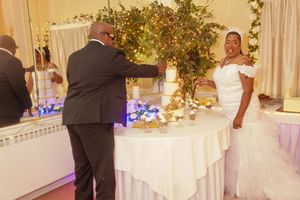 Two people stand at an elegantly decorated wedding reception table with flowers and white linens under soft lighting.