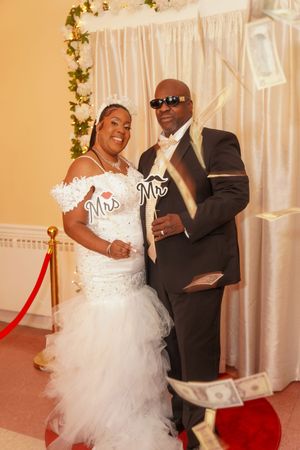 A wedding couple poses with 'Mr & Mrs' signs while money falls around them during their celebration.