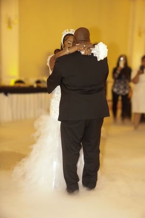 Newlyweds share their first dance in a romantic fog-filled ballroom with soft yellow lighting.