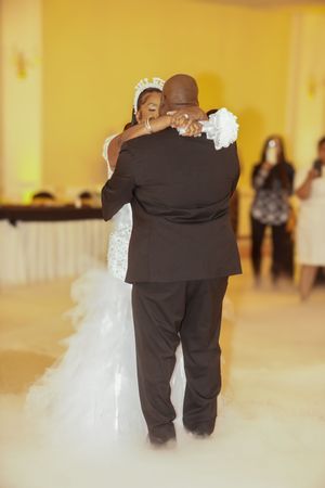 Newlyweds slow dance together at their wedding reception in a yellow-lit ballroom with fog on the dance floor.