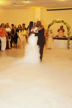 A newlywed couple shares their first dance under a floral arch while guests watch from the sidelines.