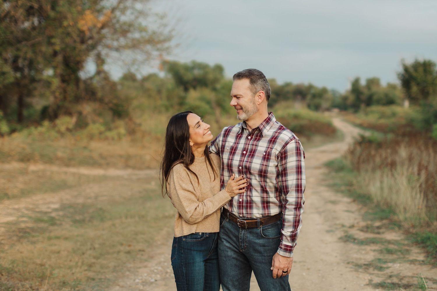 A casual outdoor family photo by a rustic wooden pergola and white fence in a lush garden setting.