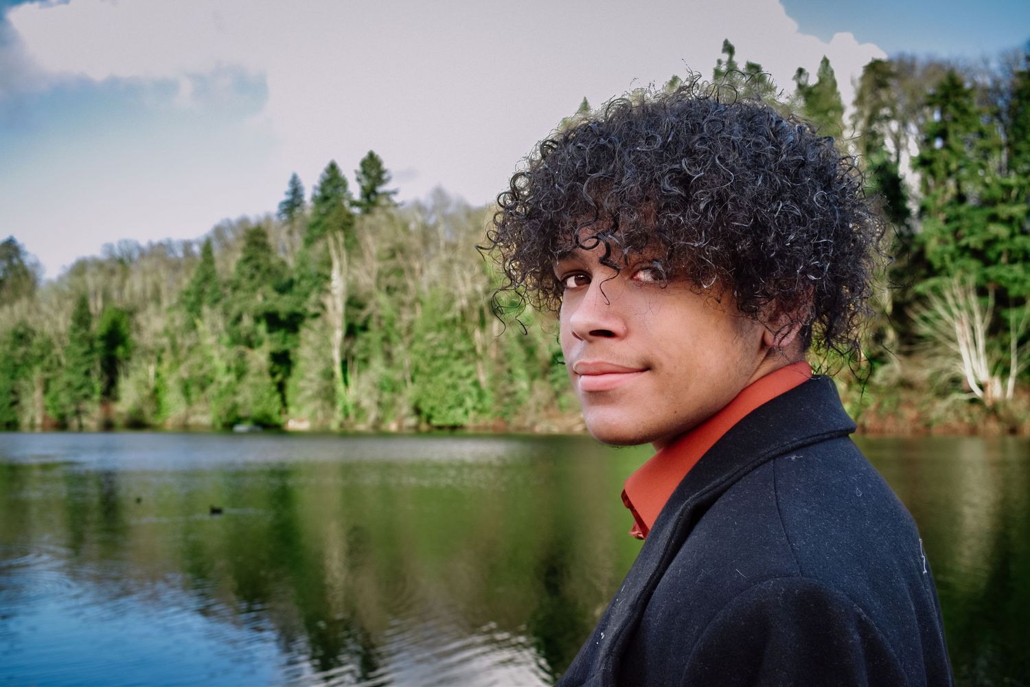 High school senior boy standing by a lake surrounded by fall colors in Seattle.