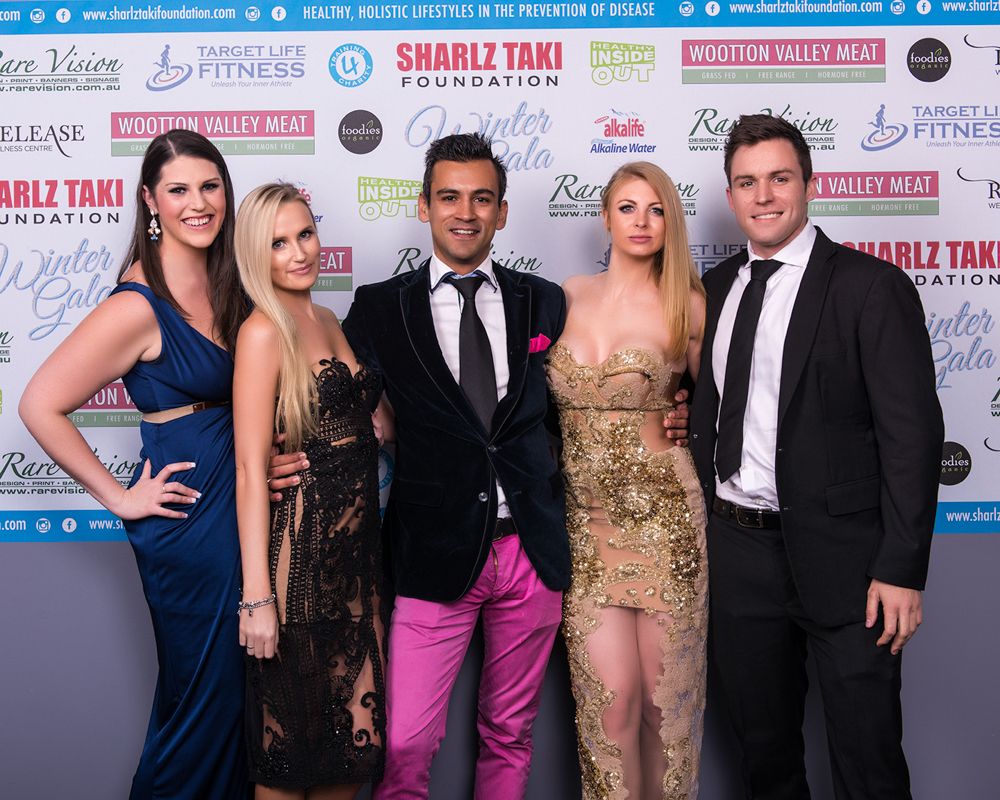 Corporate event photography Sydney. Formal event with guests posing on red carpet against branded media wall backdrop.