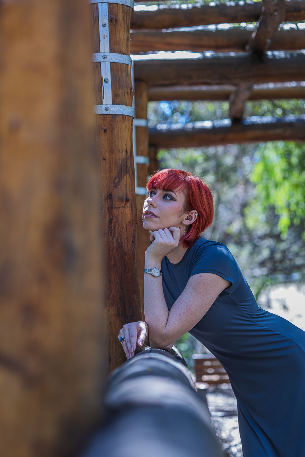 A woman rests against a wooden post, embodying a laid-back vibe in a model photoshoot.