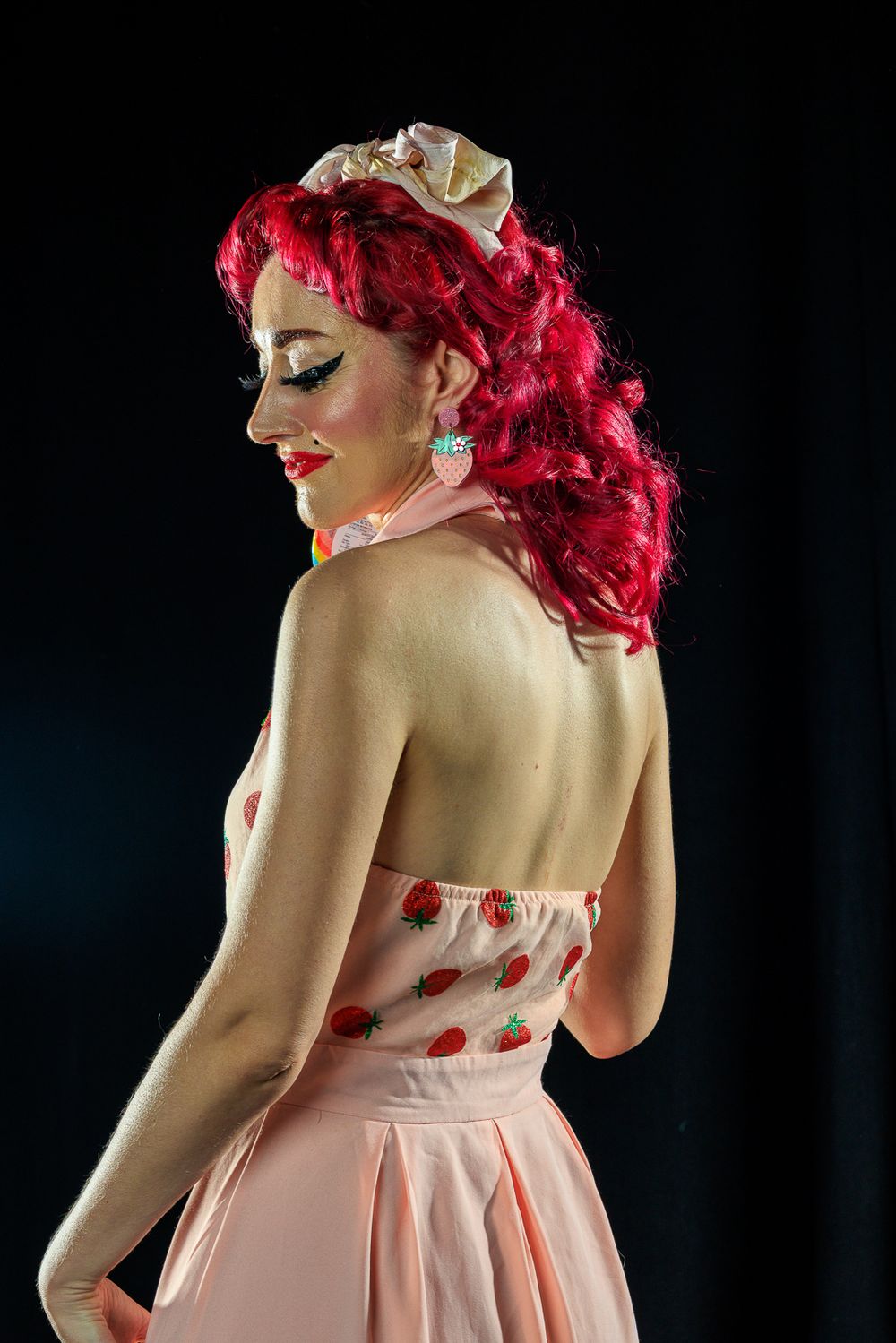 A woman with striking red hair models a pink dress in a playful pinup photoshoot, capturing a retro aesthetic.