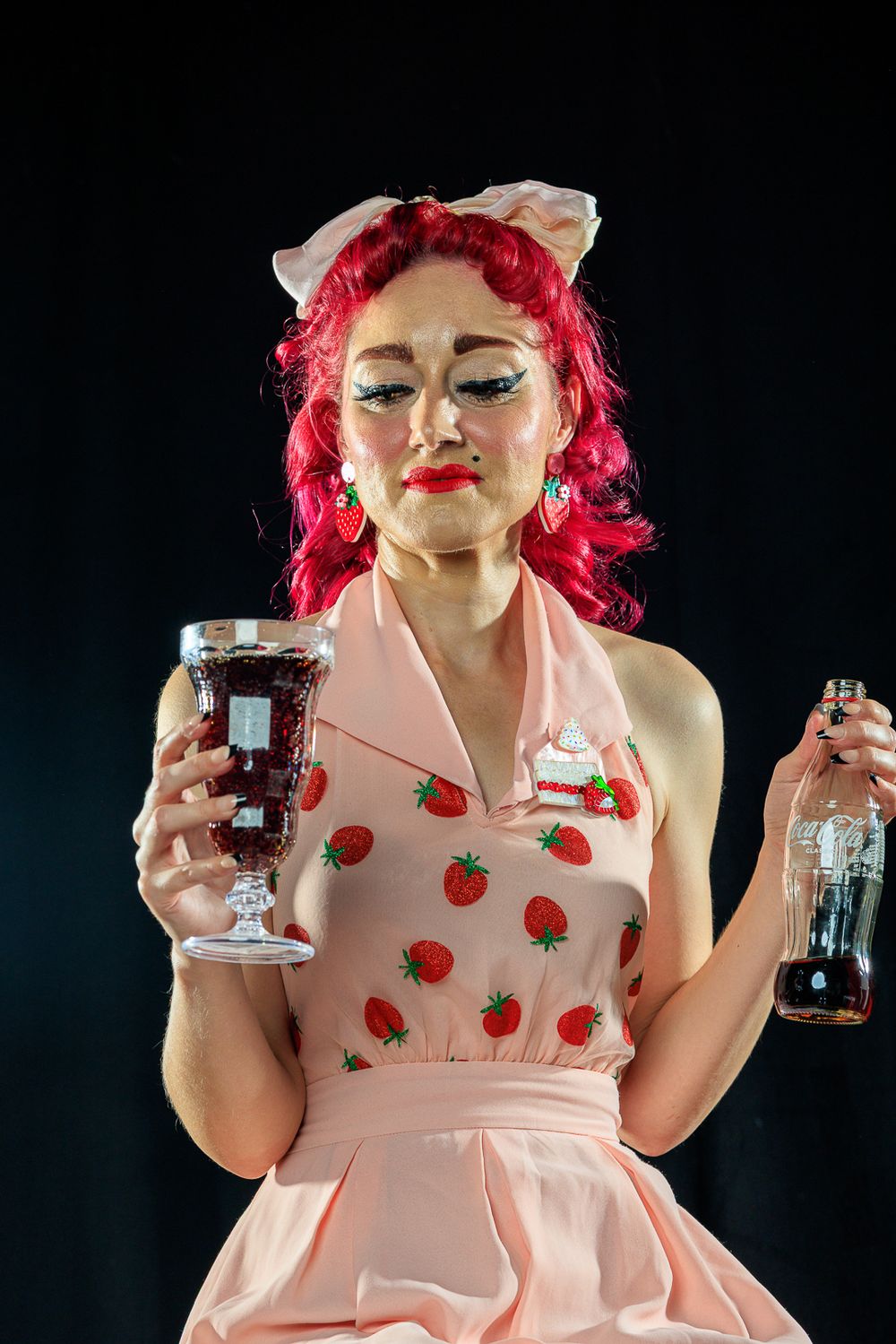 A woman with striking red hair models a pink dress in a playful pinup photoshoot, capturing a retro aesthetic.