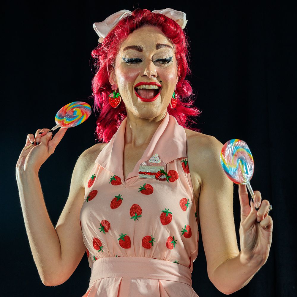 A woman with striking red hair models a pink dress in a playful pinup photoshoot, capturing a retro aesthetic.