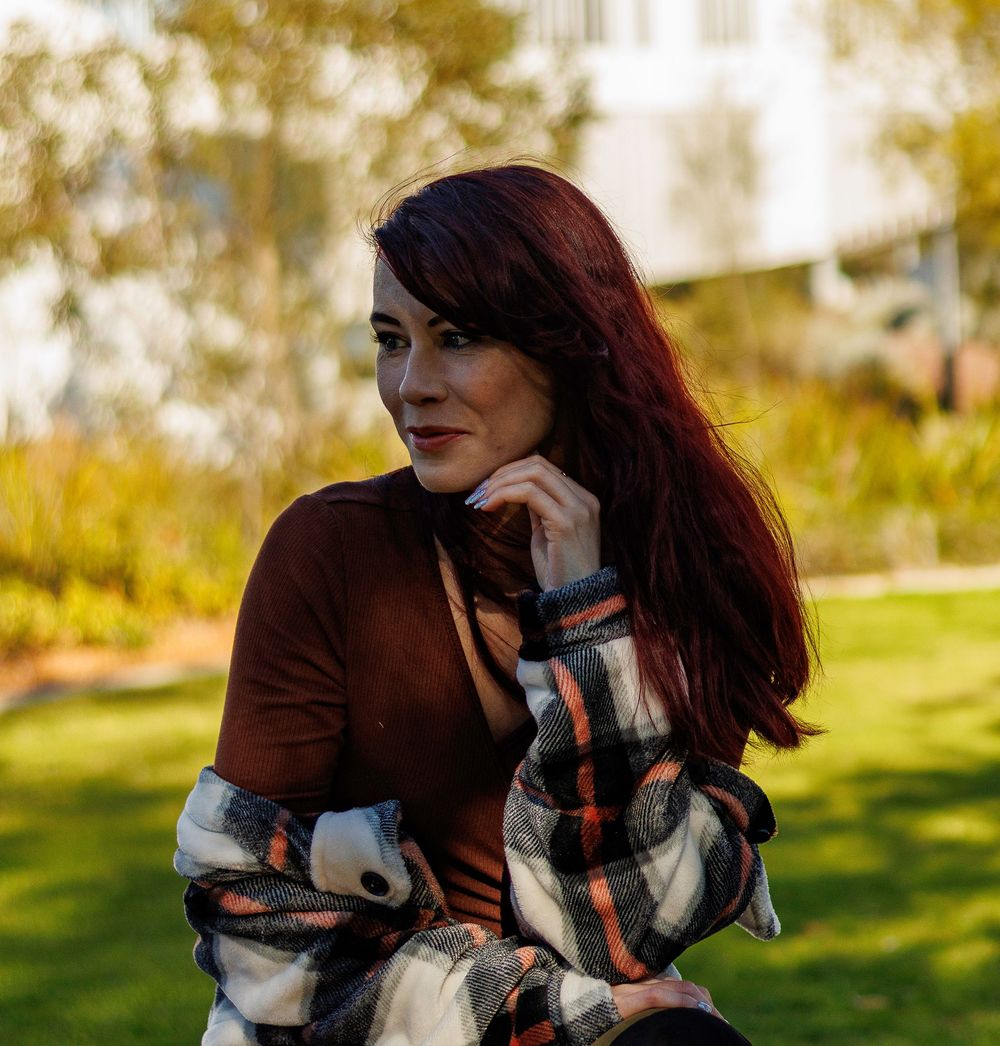A woman seating in a park, looking relaxed and cheerful, captured during a model photoshoot amidst nature.