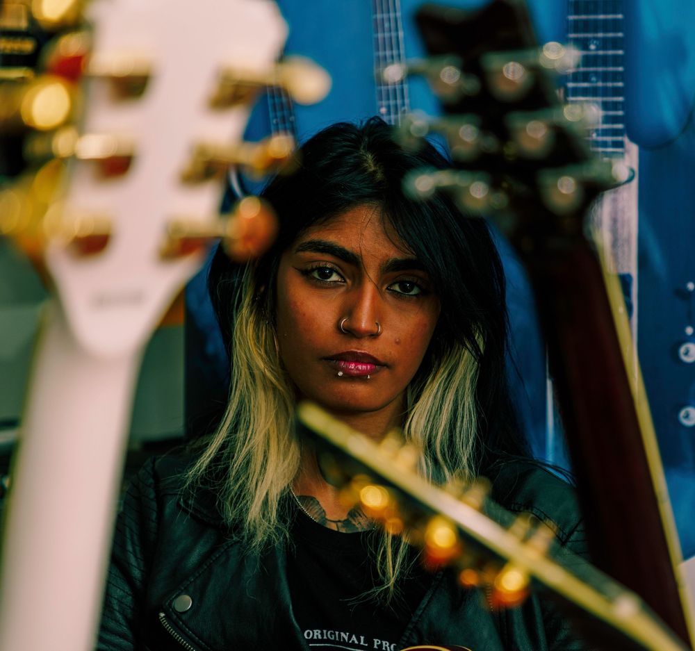 Young woman gazes intensely forward between the blurred necks of two guitars against a blue background.