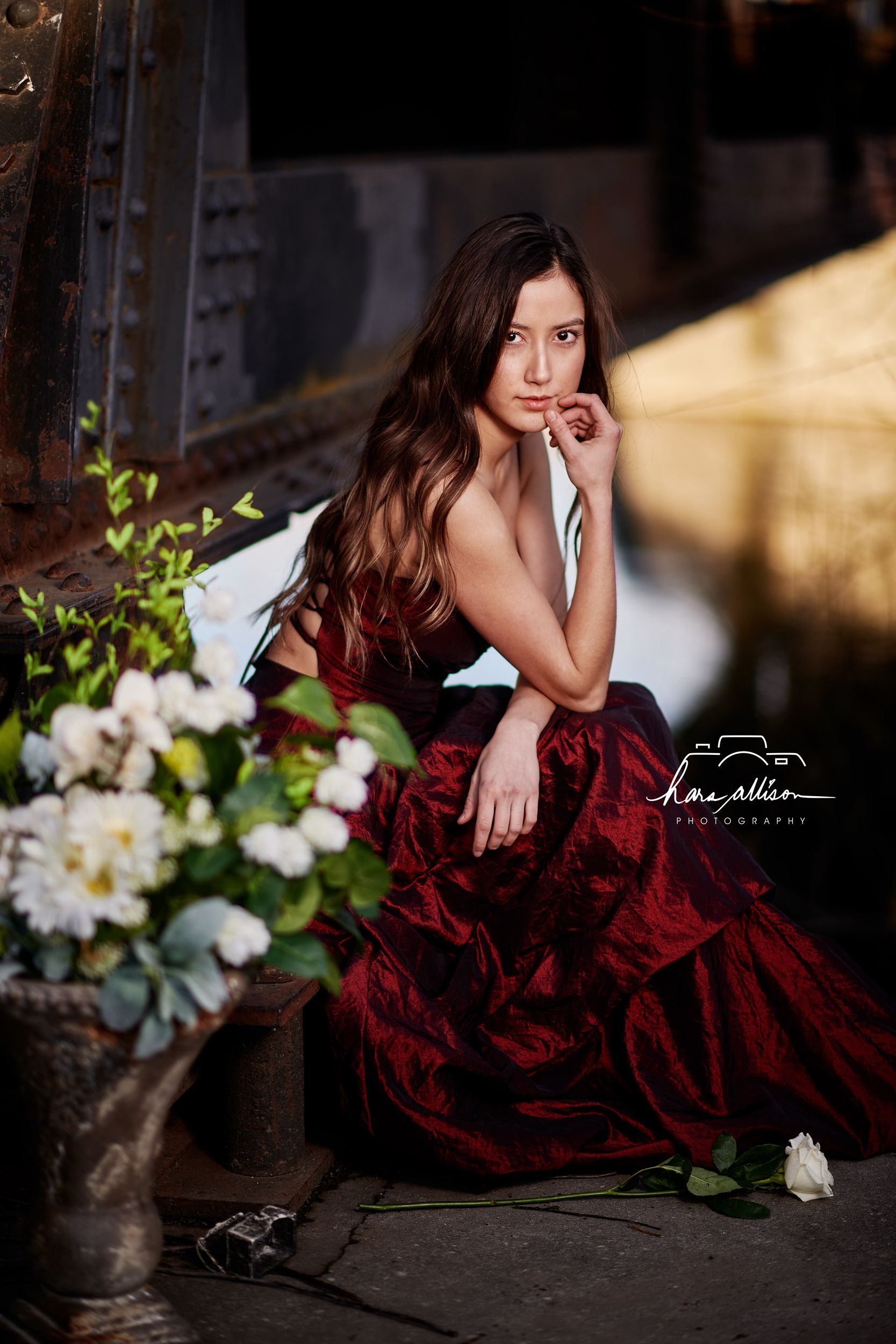 A dramatic portrait shoot featuring a deep burgundy velvet gown next to white flowers in natural lighting.