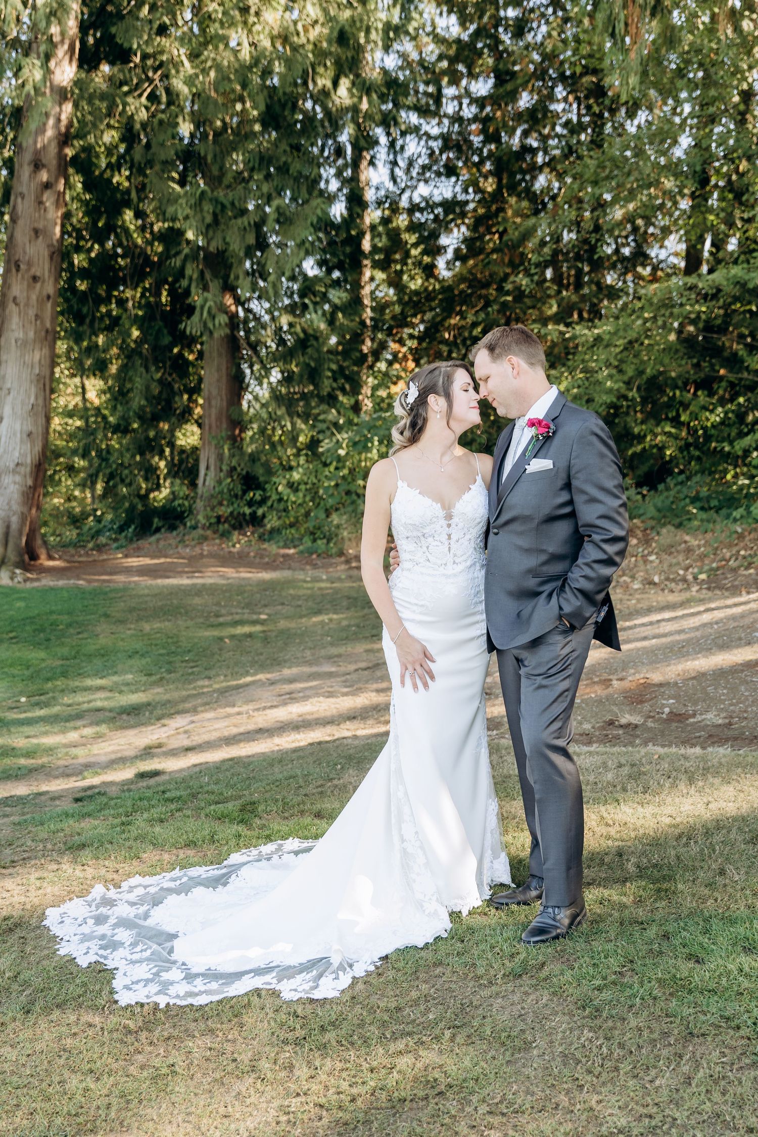 A romantic wedding couple poses together on a grassy hillside with a flowing white dress train.