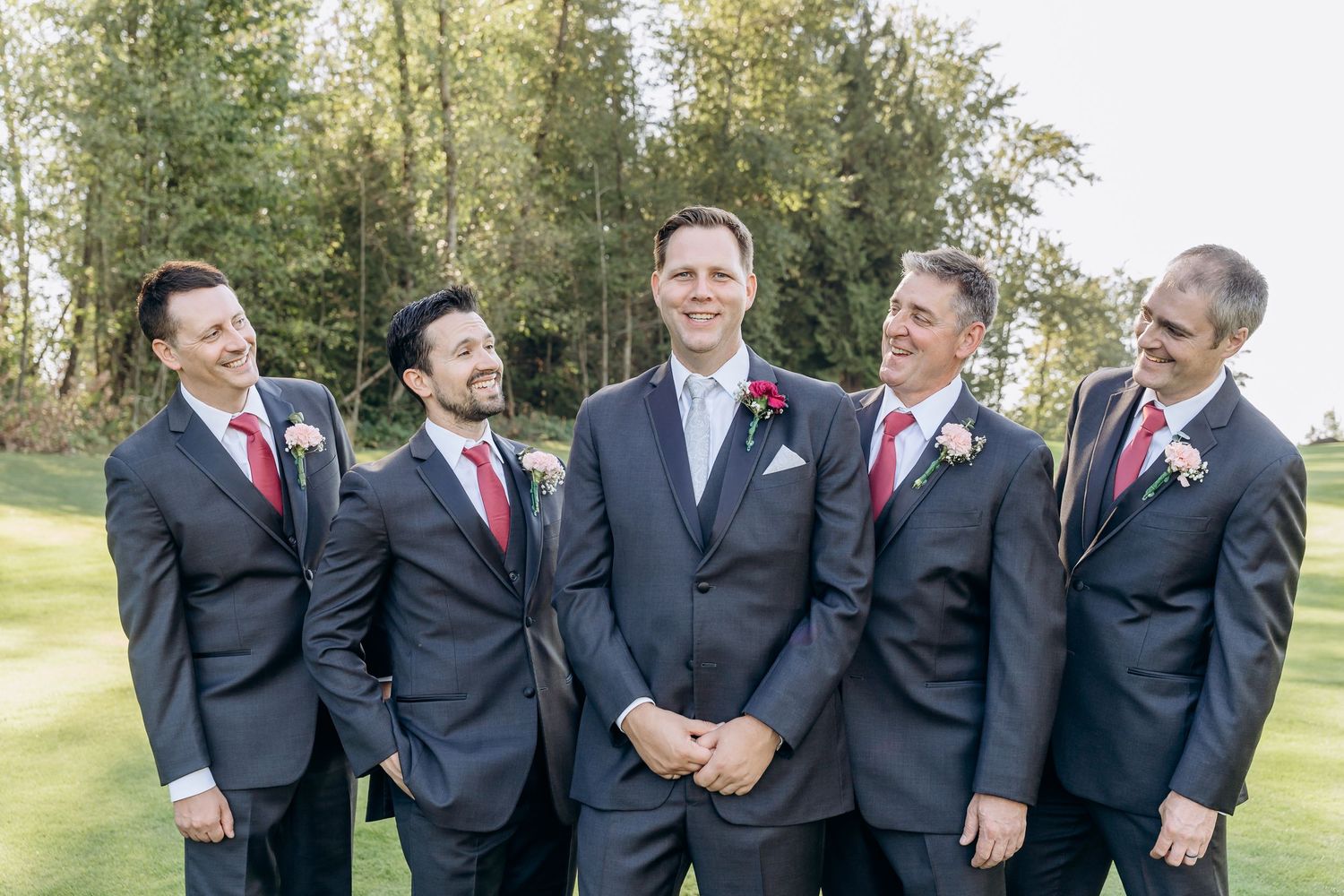 Groomsmen in black suits with red ties share laughs during wedding photo session.