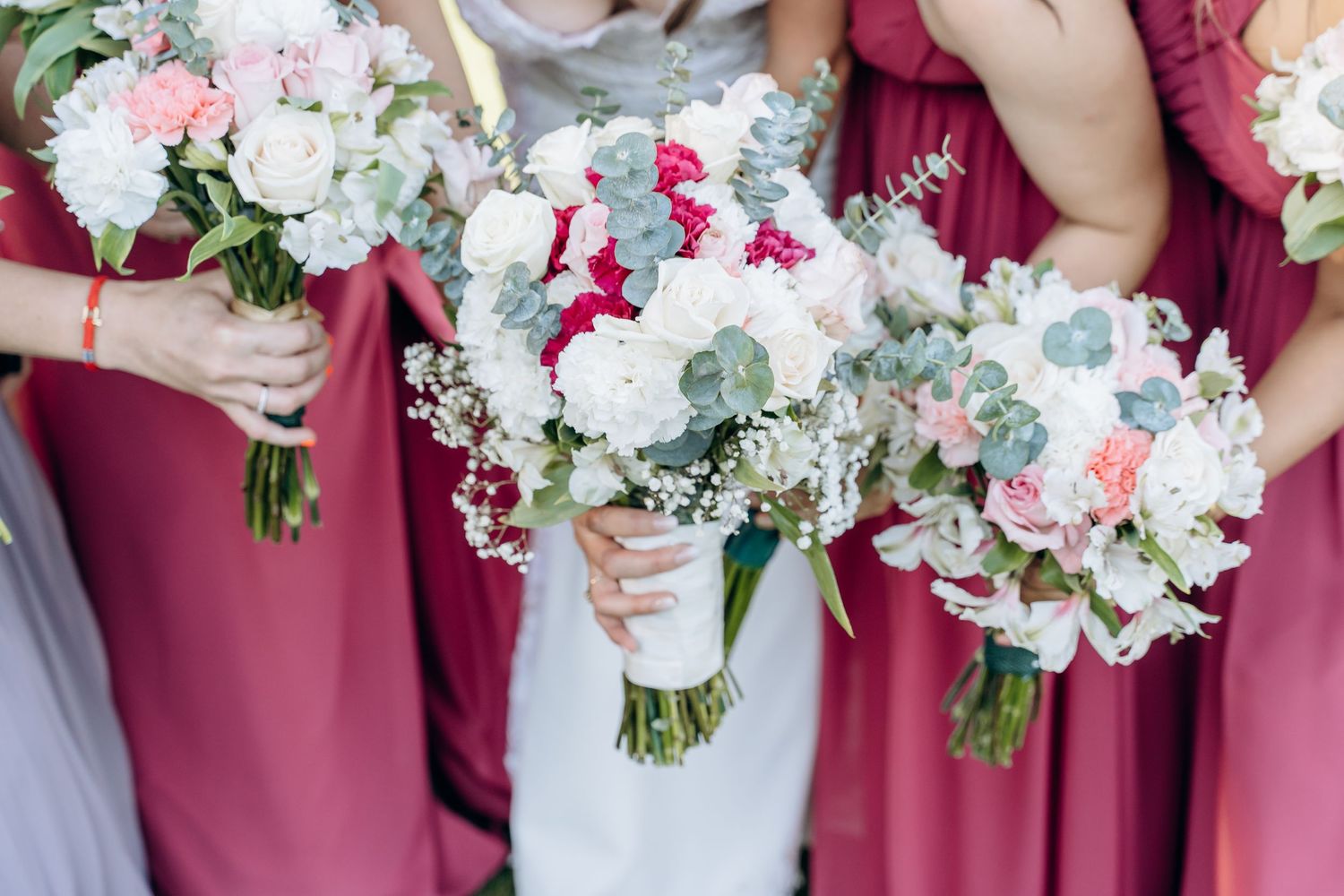 Close-up of elegant white and pink wedding bouquets held by bridesmaids in burgundy dresses.
