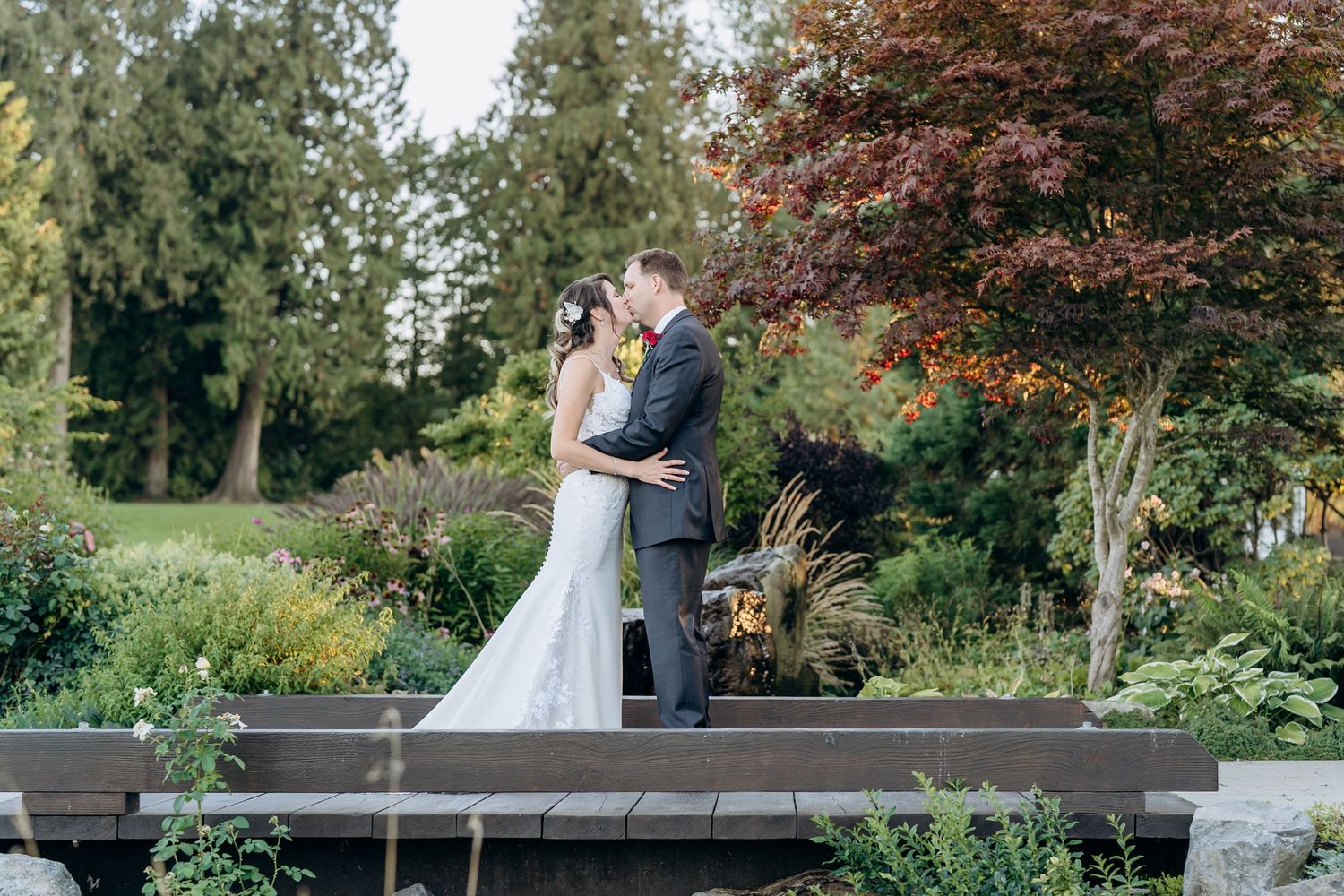 A wedding ceremony takes place under a wooden pergola with autumn foliage in the background.