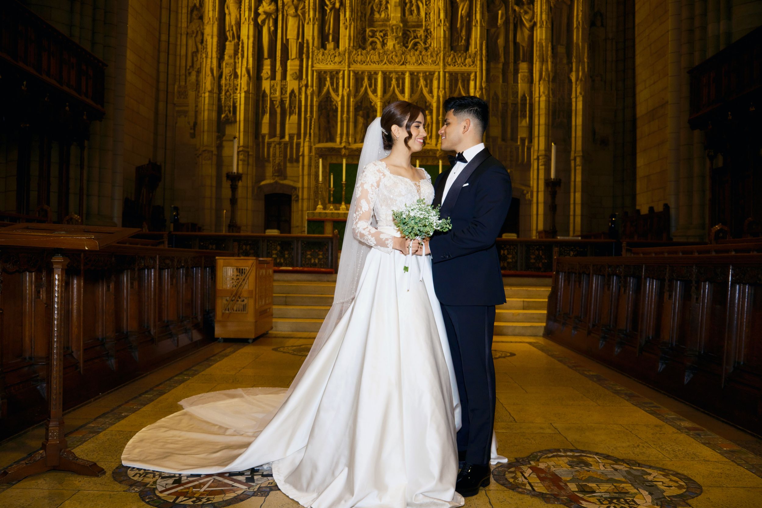 Wedding couple standing in ornate church aisle with gothic architecture and golden altar.
