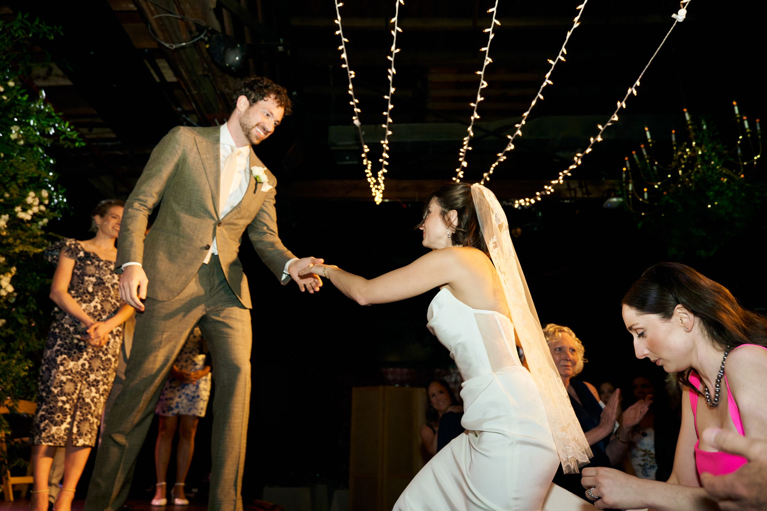 Dance celebration at a reception with string lights hanging overhead as couple moves across the floor.