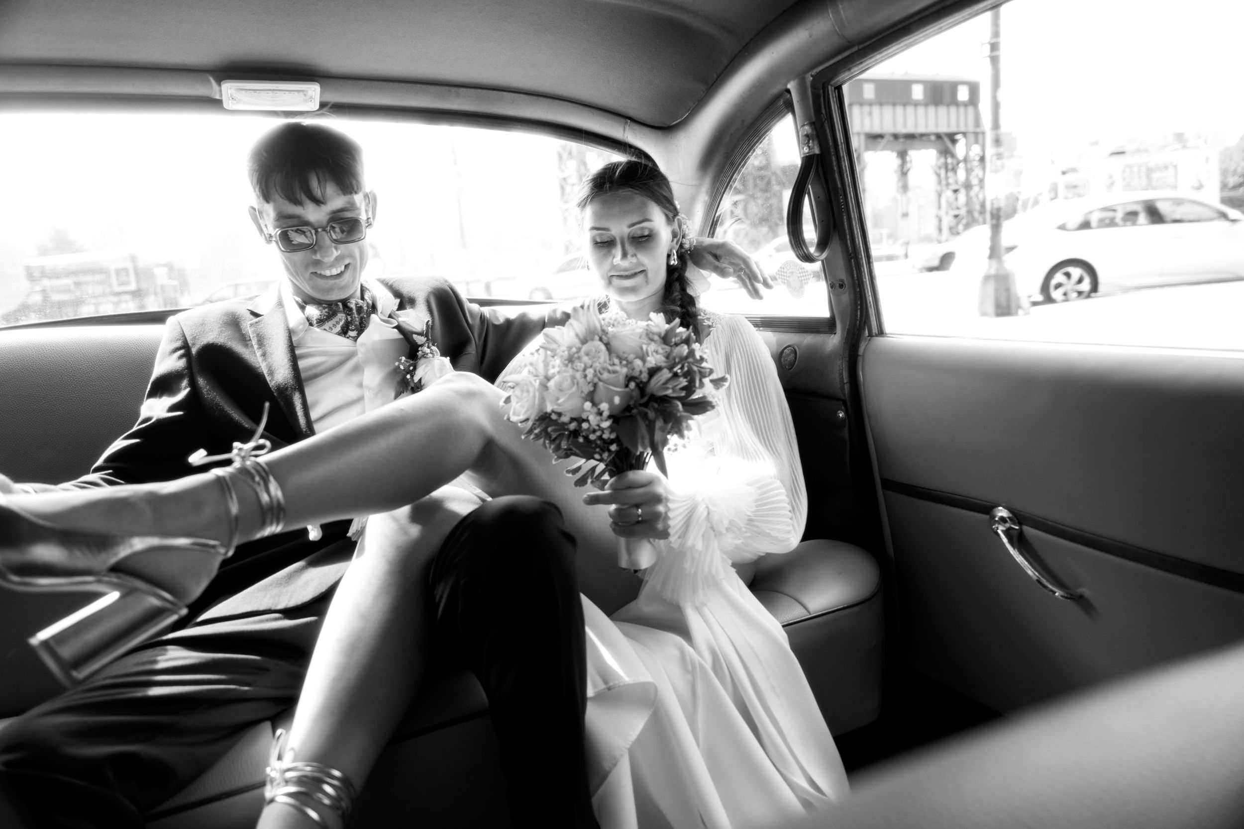 Wedding party riding in a car together, captured in candid black and white photography.