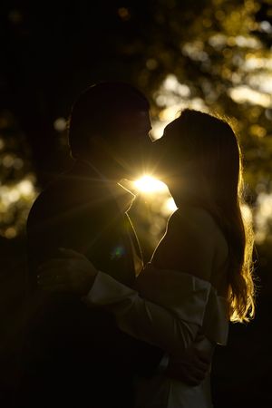 Silhouetted couple embracing at sunset with golden sunlight between them.