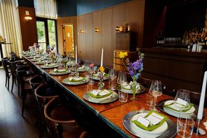 Elegant restaurant table setting with place settings, wine glasses and purple floral centerpieces along a wooden dining table.