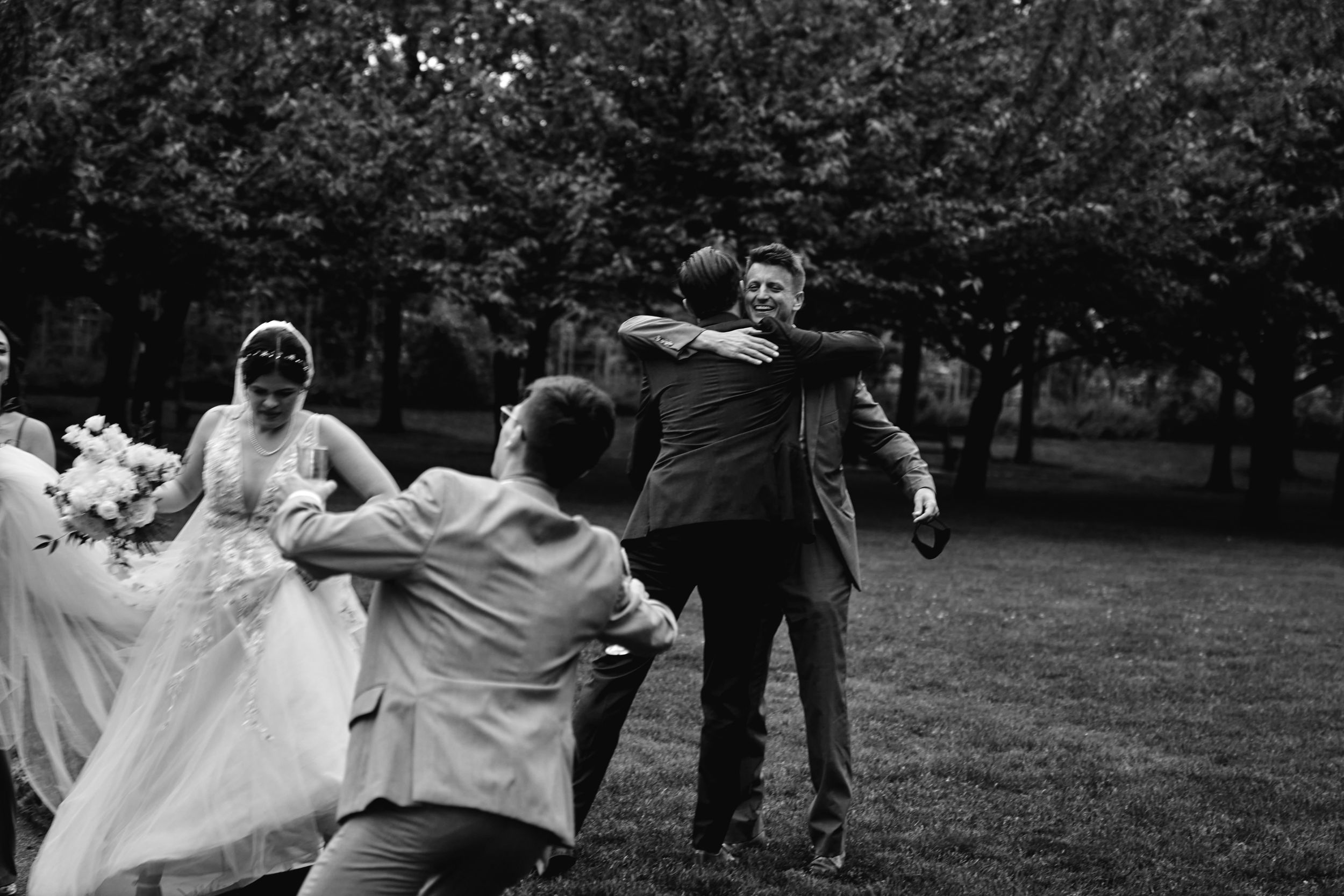 Black and white photo of wedding party playing and dancing together in an outdoor garden setting.