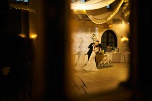 First dance at wedding reception viewed through doorway with romantic lighting and draped fabric.