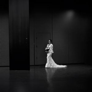 Dramatic black and white photo of bride in flowing gown against dark background.