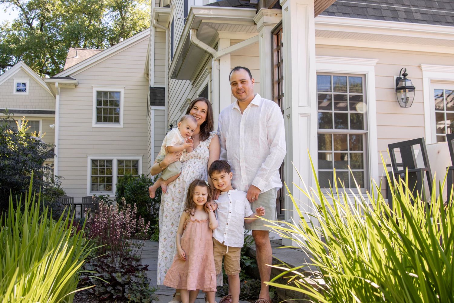 A family of five smiles for a portrait outside of their home.