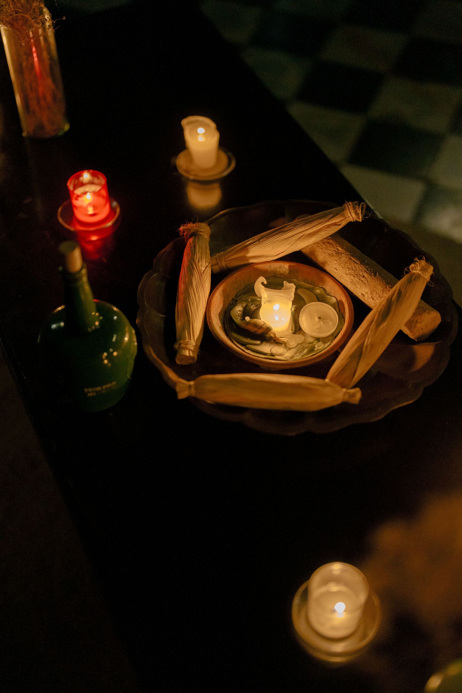 Lit candles cast a warm glow on wooden sticks arranged in a mystical pattern on a dark surface.