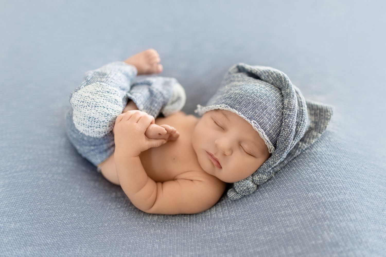 Sleeping newborn wearing gray knit hat and diaper lying on soft blue backdrop in photography studio. Photos by Tampa's DigitalMyst Photo