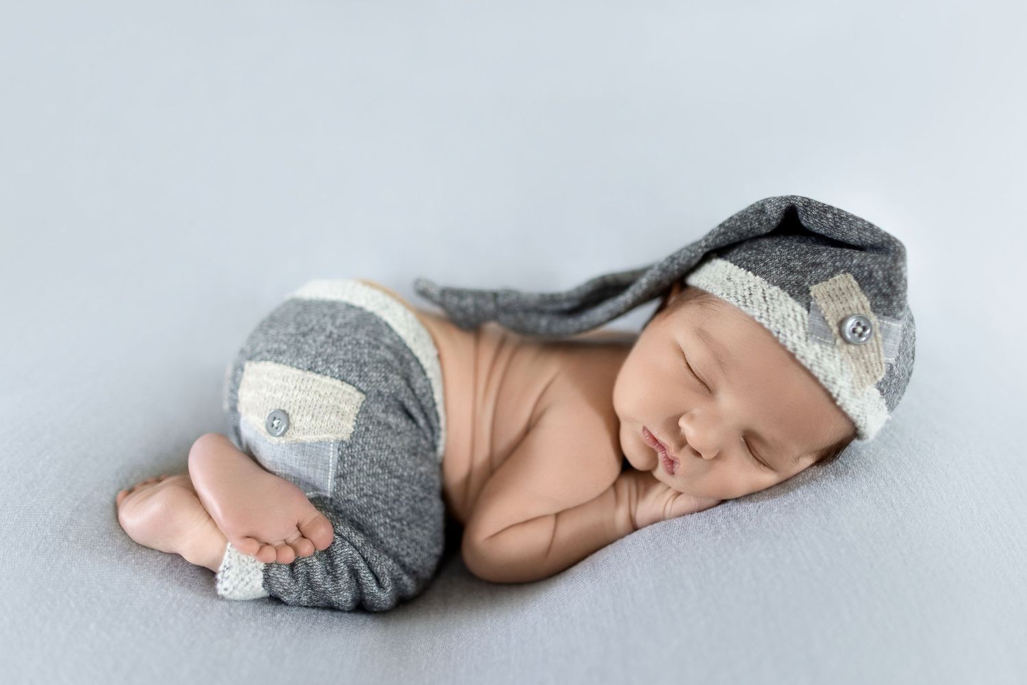 Tiny newborn in grey outfit curled up asleep on light colored backdrop. Photos by Tampa Photographer DigitalMyst Photography