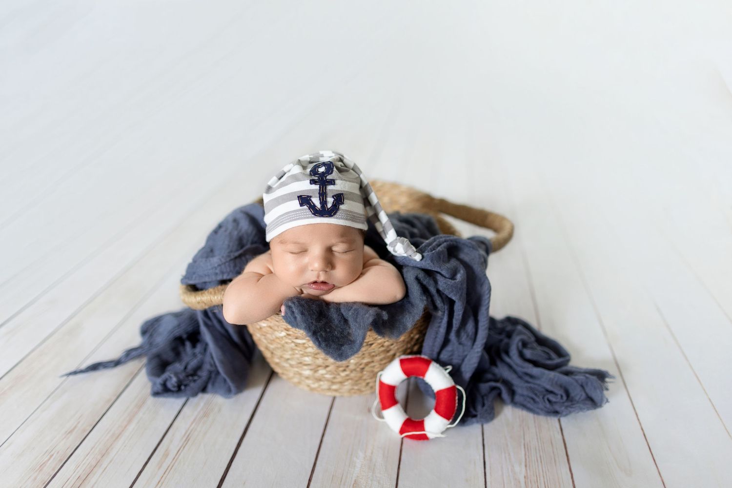Nautical themed newborn photo with blue fabric, lifesaver prop and wooden floor setting. Photos by Tampa Photographer DigitalMyst