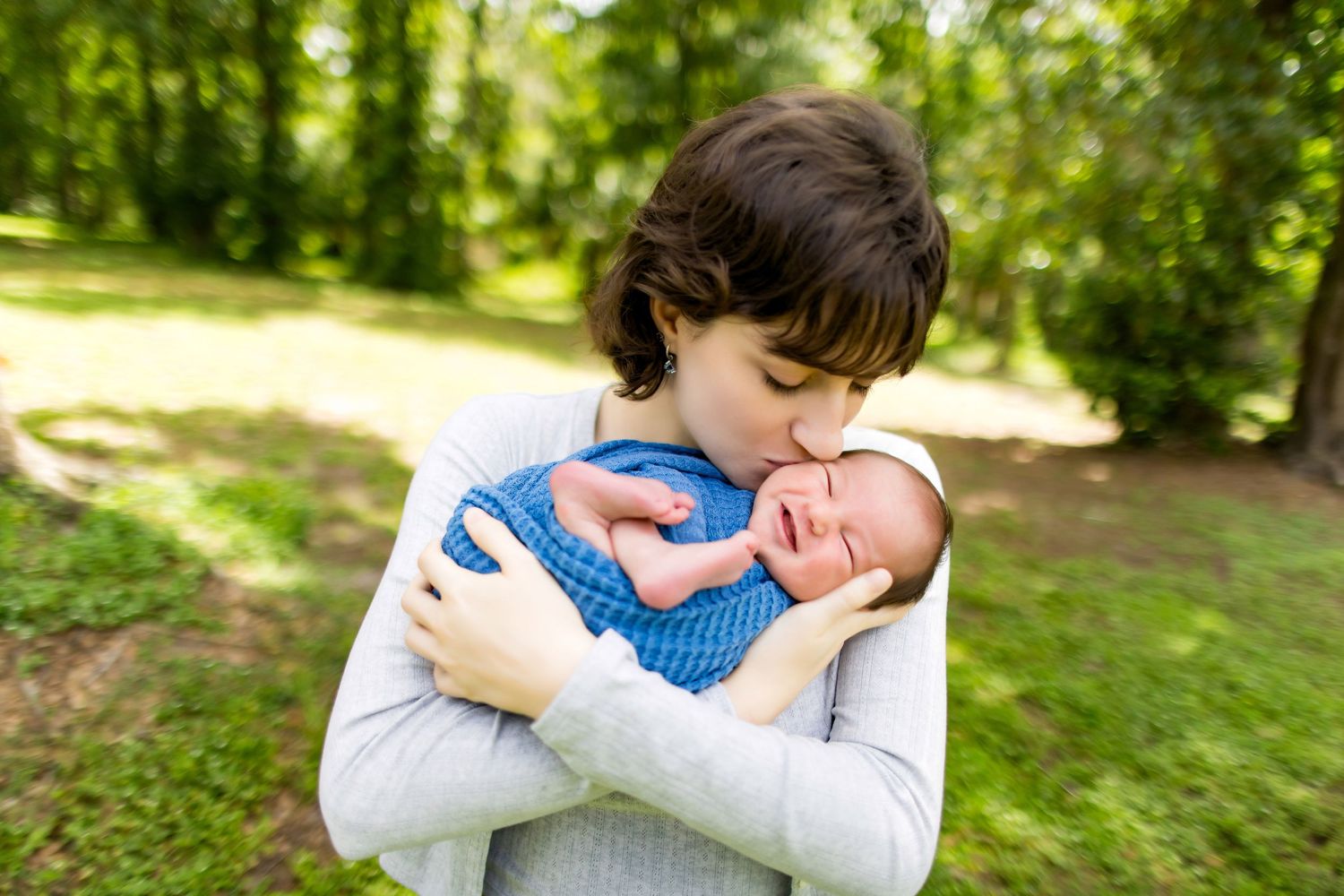 A sweet outdoor moment captured showing affection towards a baby in a blue outfit on a sunny day. Photos by Tampa Photographer DigitalMyst