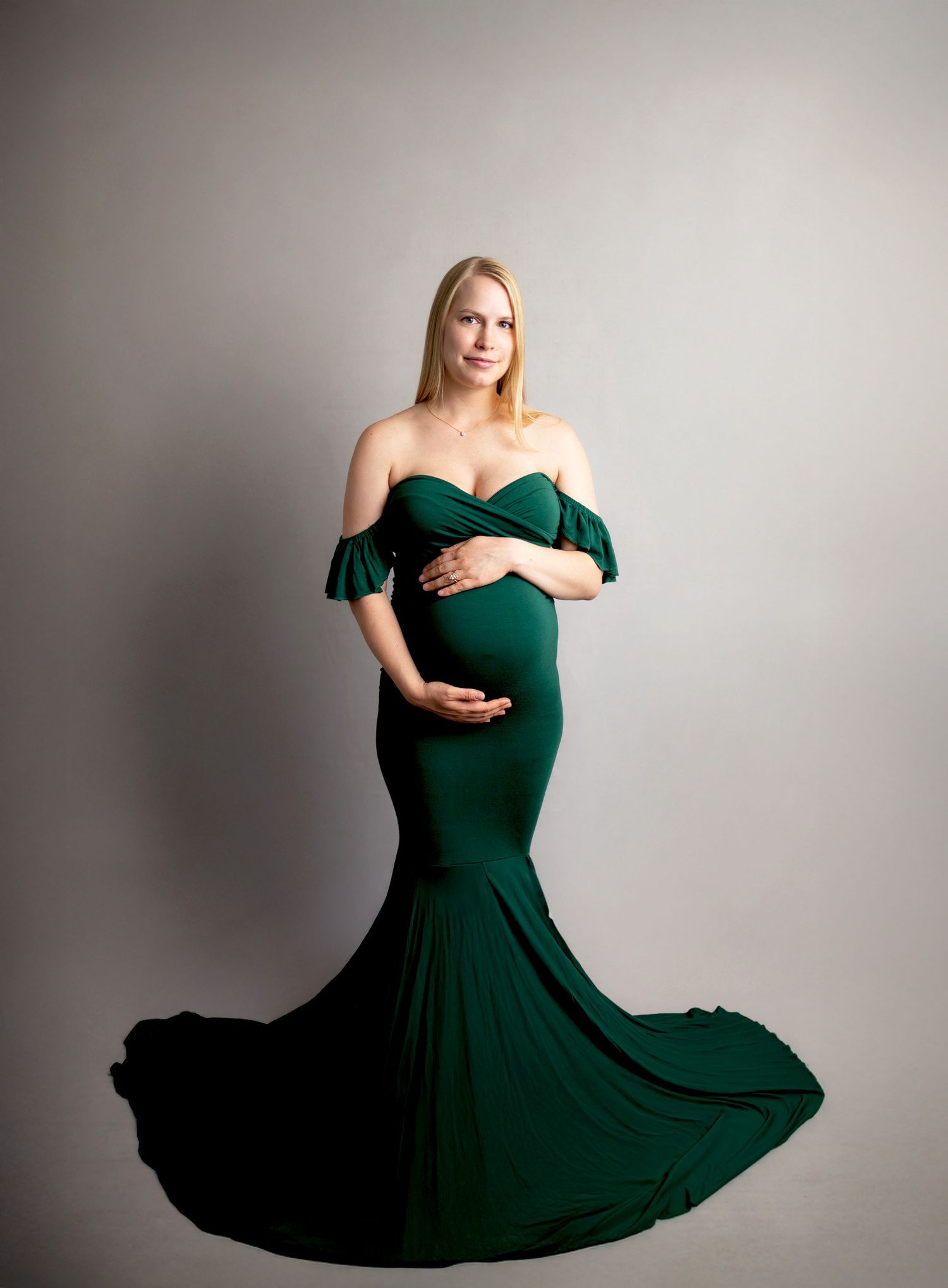 Elegant green maternity gown with off-shoulder ruffled sleeves and dramatic mermaid silhouette with flowing train.