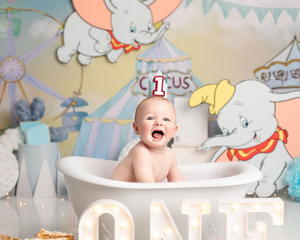 Baby sitting in bathtub with circus themed backdrop and large illuminated 'ONE' letters. ipswich cake smash photographer, dumbo the elephant