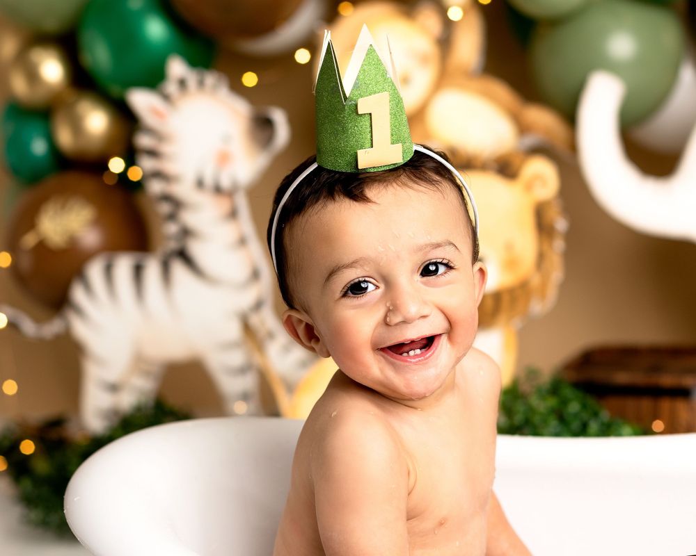 Smiling baby wearing green party hat against safari themed balloon backdrop with tiger decoration. Pallara cake smash photographer, safari t
