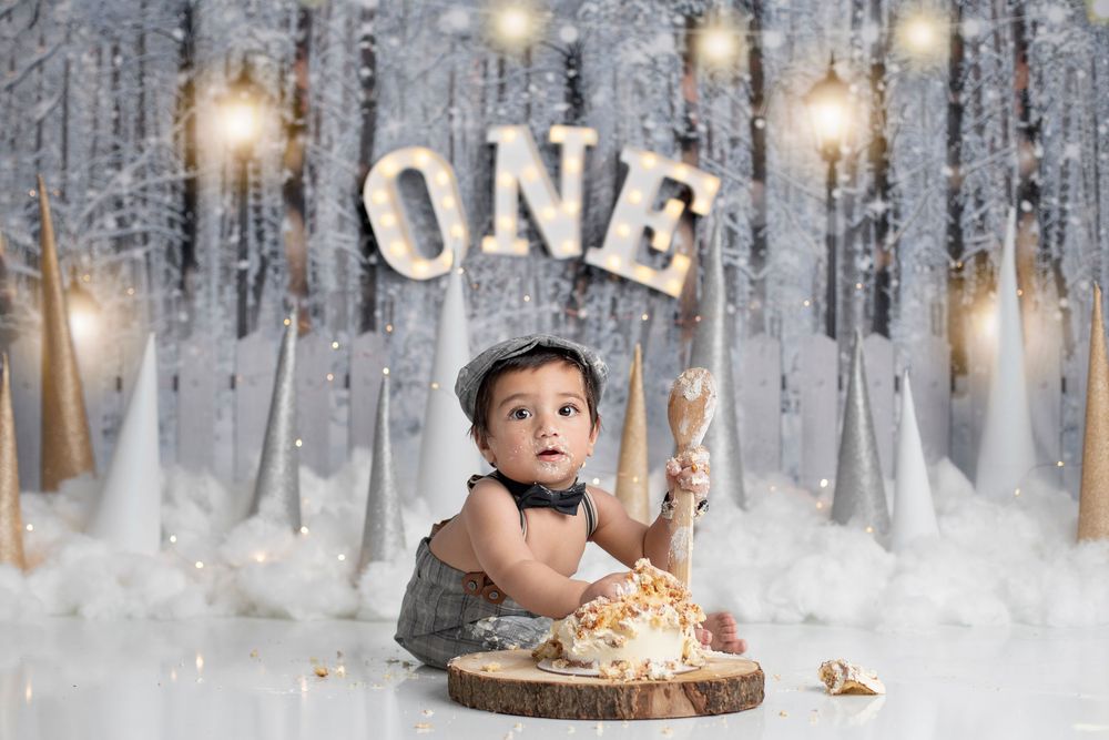 A winter-themed first birthday cake smash photo with sparkly lights, white decor, and a wooden slice cake stand. forest lake cake smash