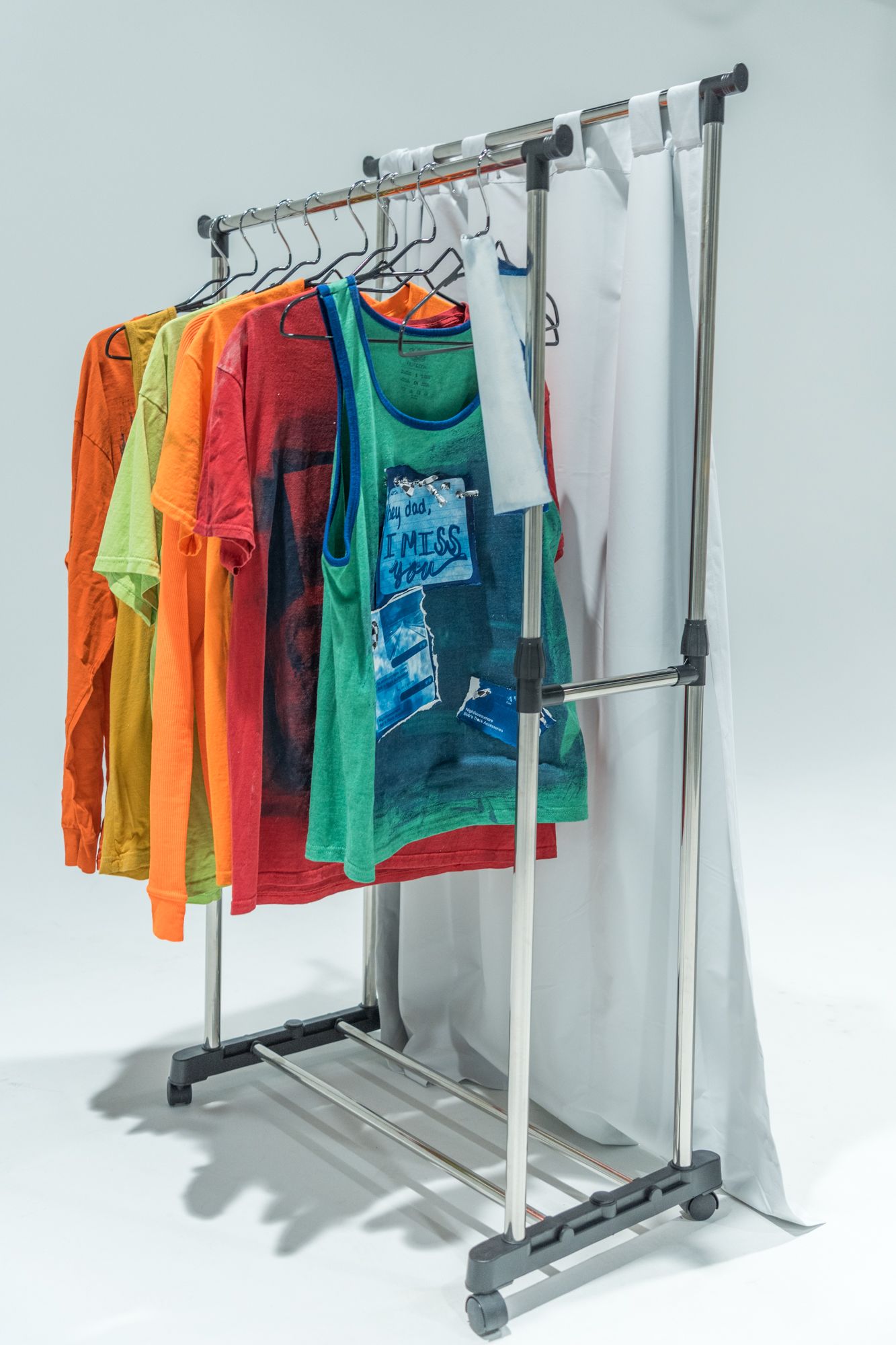 Colorful t-shirts hanging on a portable clothing rack against white background.